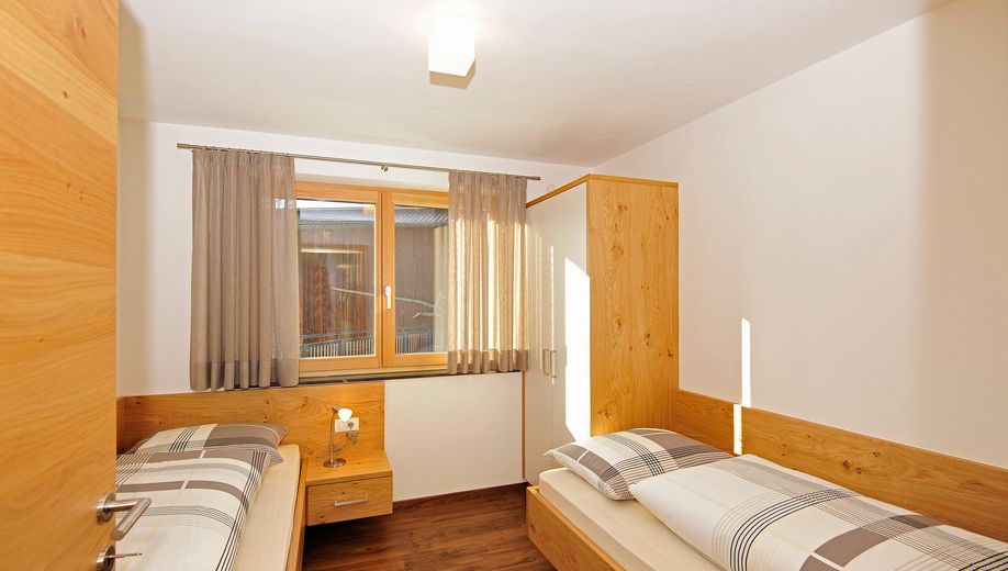 Kleines Schlafzimmer mit zwei Einzelbetten, Holzmöbeln und Fenster mit Vorhängen.