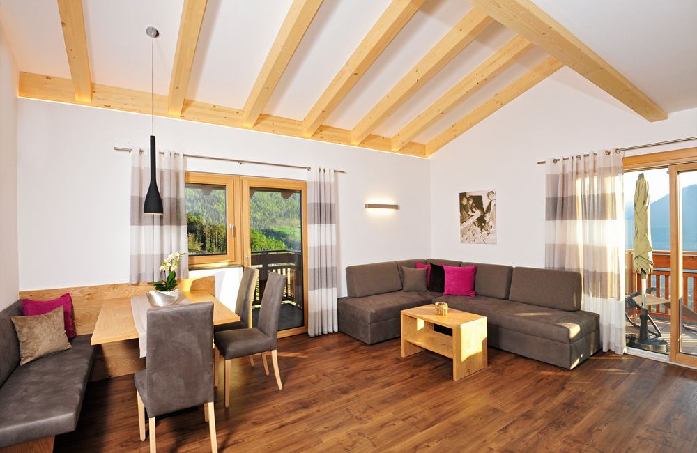 Helles Wohnzimmer mit Holzbalkendecke, Essbereich und Sofaecke mit bunten Kissen.