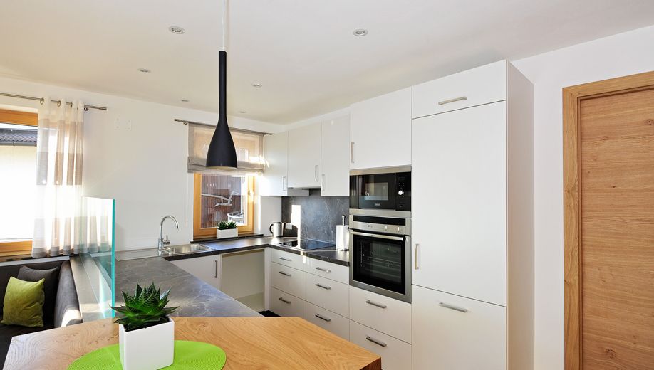 Moderne weiße Küche mit schwarzen Arbeitsplatten und Holzdetails.