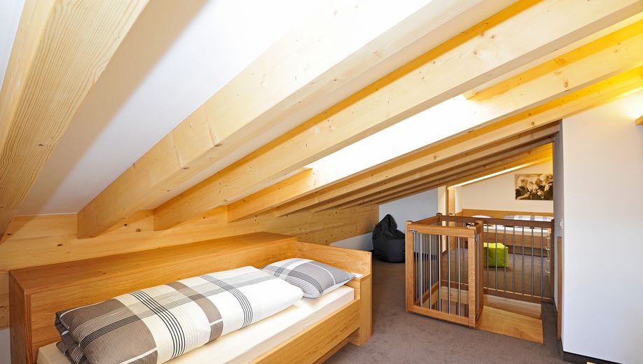Dachboden mit geneigter Holzdecke, Bett und Treppenschutzgitter