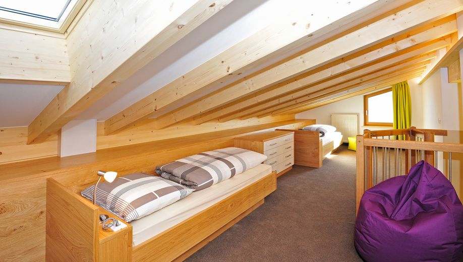 Schlafzimmer im Dachgeschoss mit zwei Holzbettgestellen, Dachfenster, hellem Holz und lila Sitzsack.