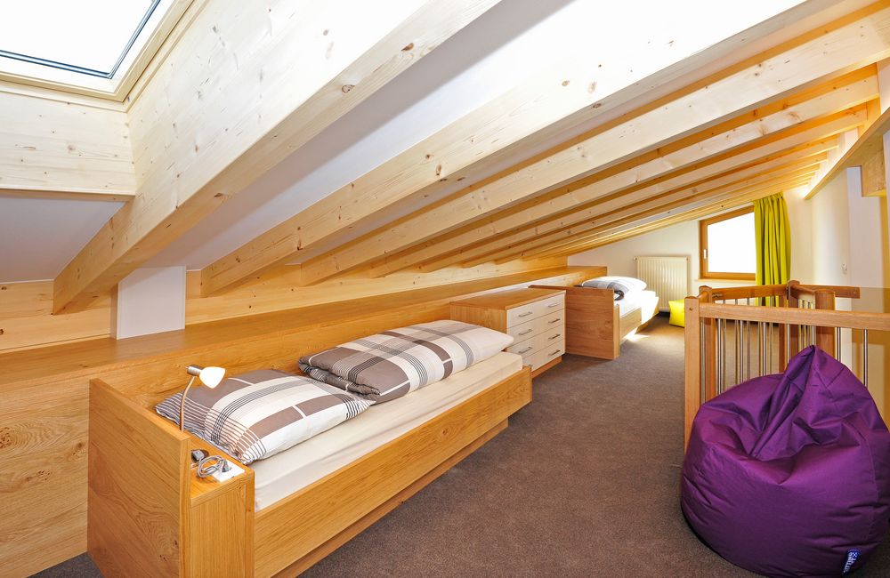 Schlafzimmer im Dachgeschoss mit zwei Holzbettgestellen, Dachfenster, hellem Holz und lila Sitzsack.