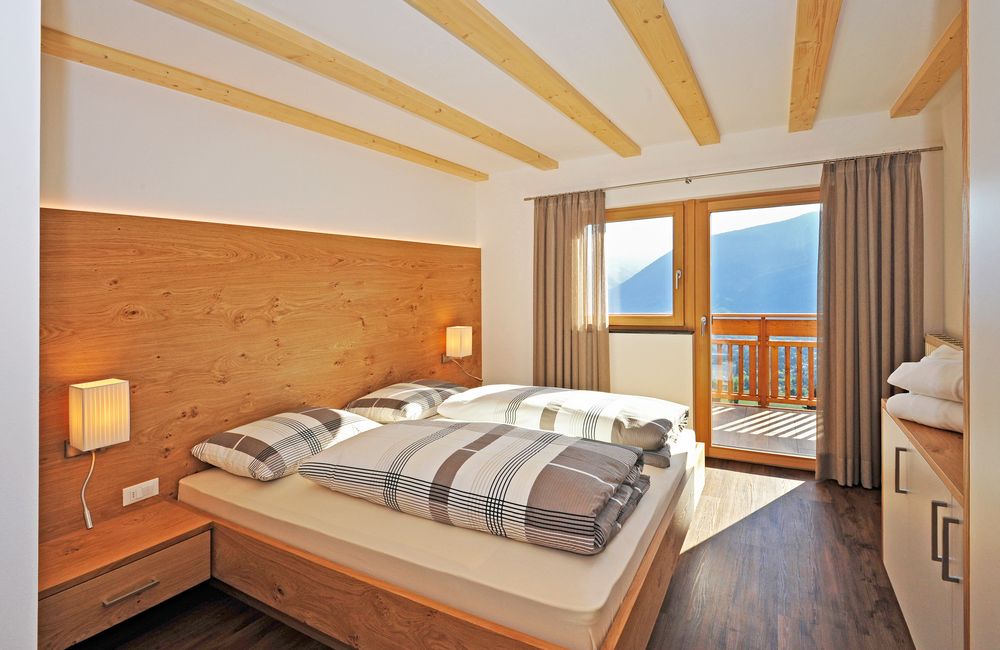 Modernes Schlafzimmer mit Holzbett, Panoramafenster und Bergblick