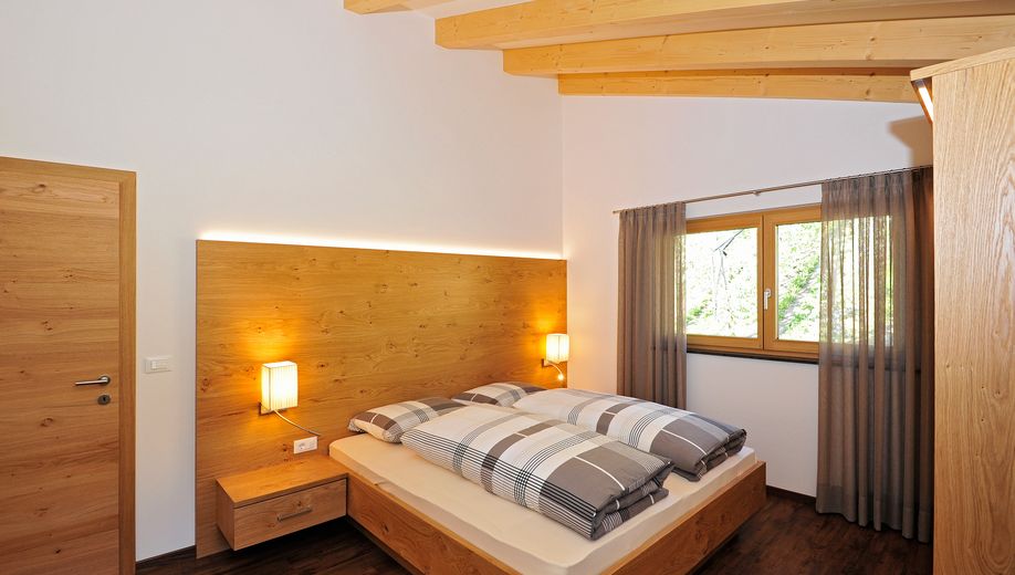 Hell eingerichtetes Schlafzimmer mit Holzmöbeln und großem Fenster.