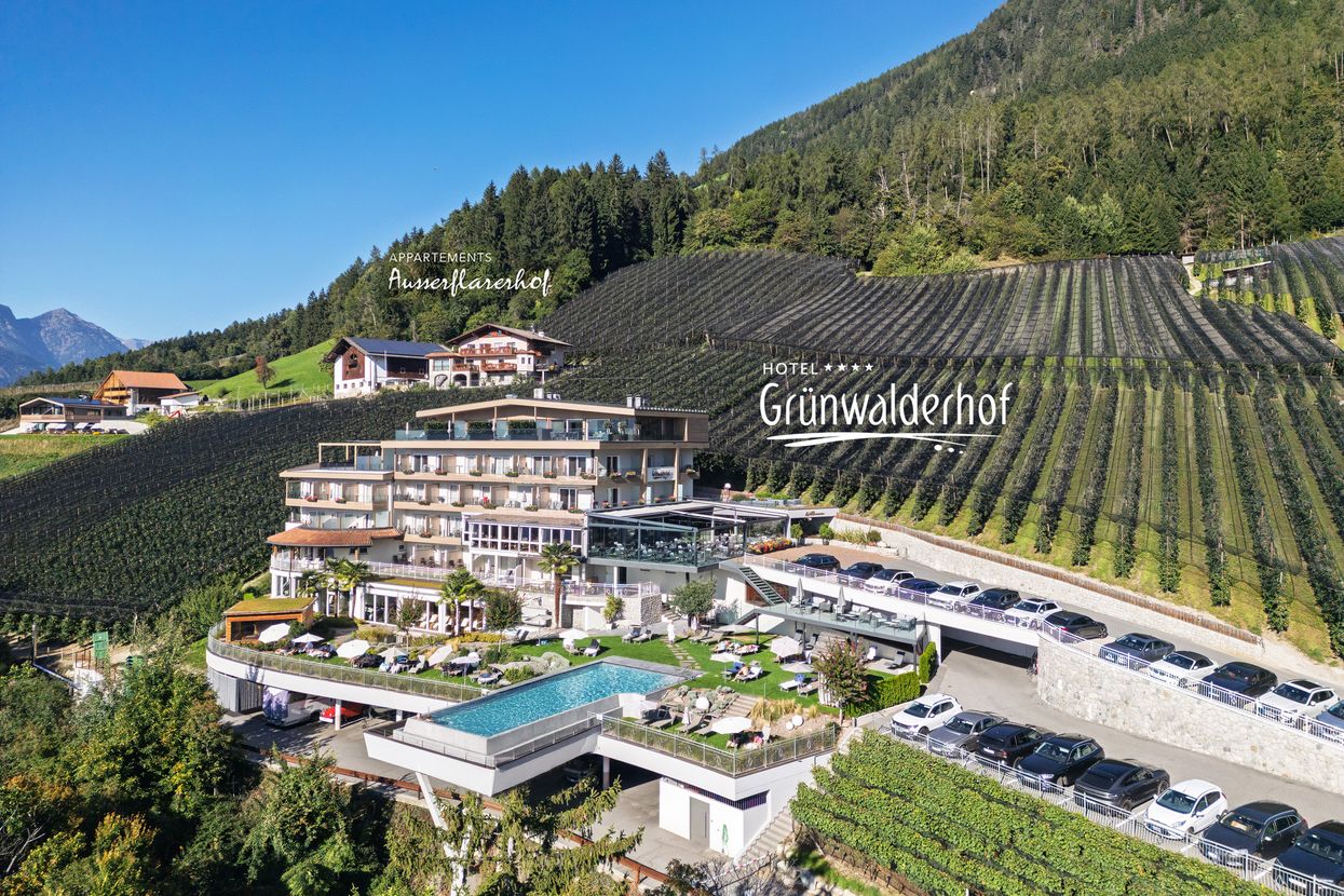 Hotel Grünwalderhof mit Außenpool in einer bergigen Landschaft mit Weinbergen.