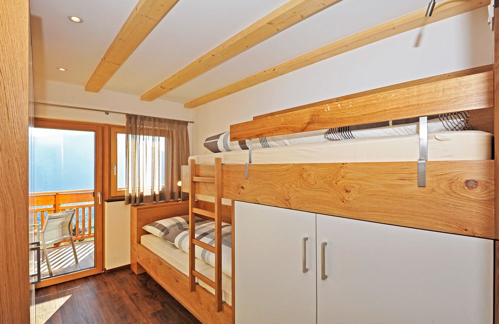 Kleines Schlafzimmer mit Etagenbett aus Holz und Balkon mit Stühlen